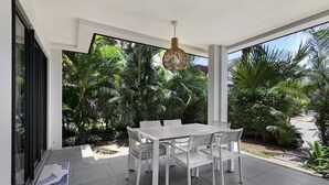 A modern outdoor dining area with a white table and chairs, surrounded by lush greenery and a clear view of the street. - Choisy Les Bains M2 (Mont Choisy)