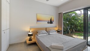 A modern bedroom with a large bed, a nightstand with a lamp, a painting of a sailboat on the wall, and a view of greenery through a sliding glass door. - Choisy Les Bains M2 (Mont Choisy)