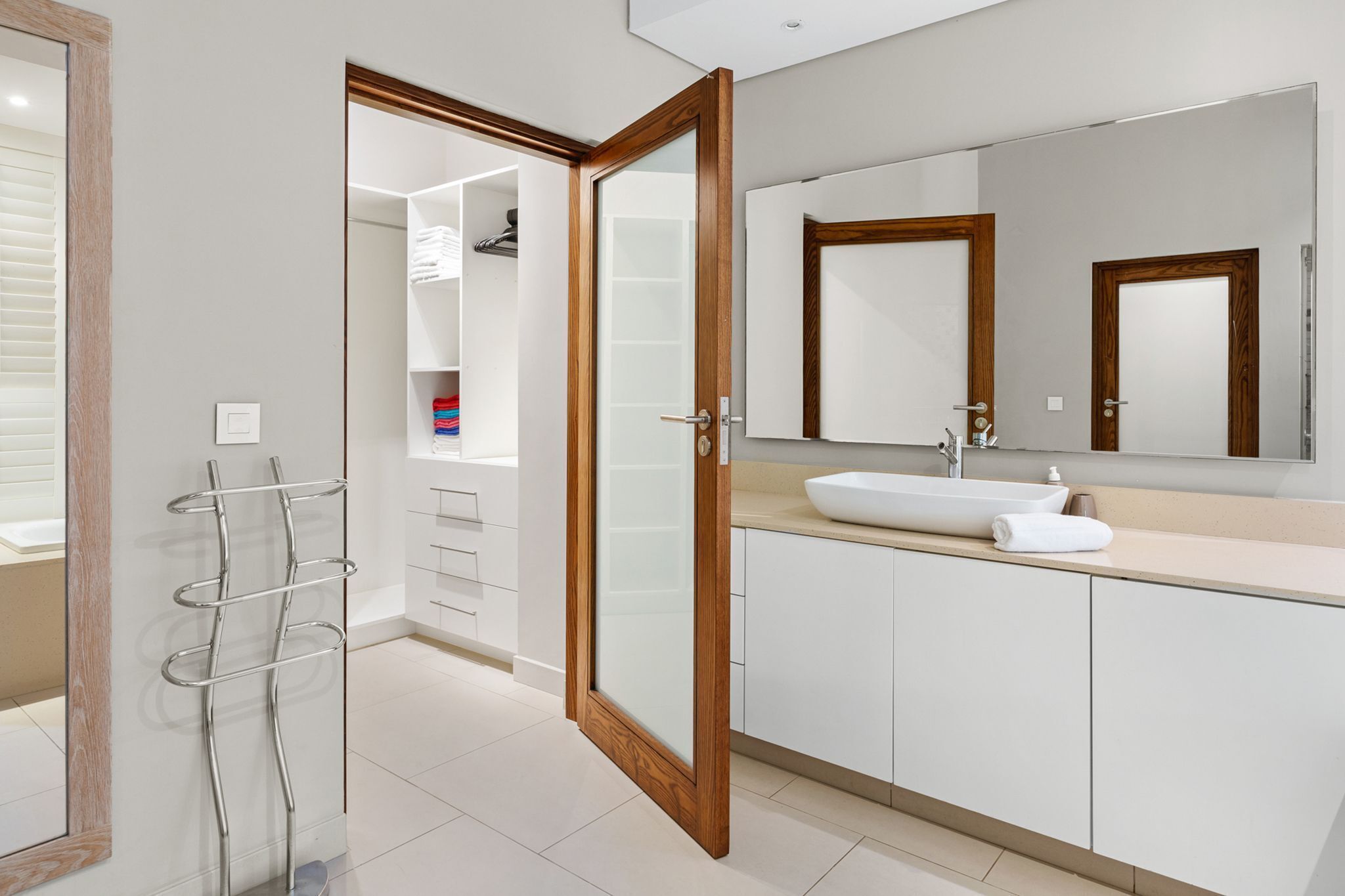 A modern bathroom with a large mirror, white cabinets, and a towel rack.