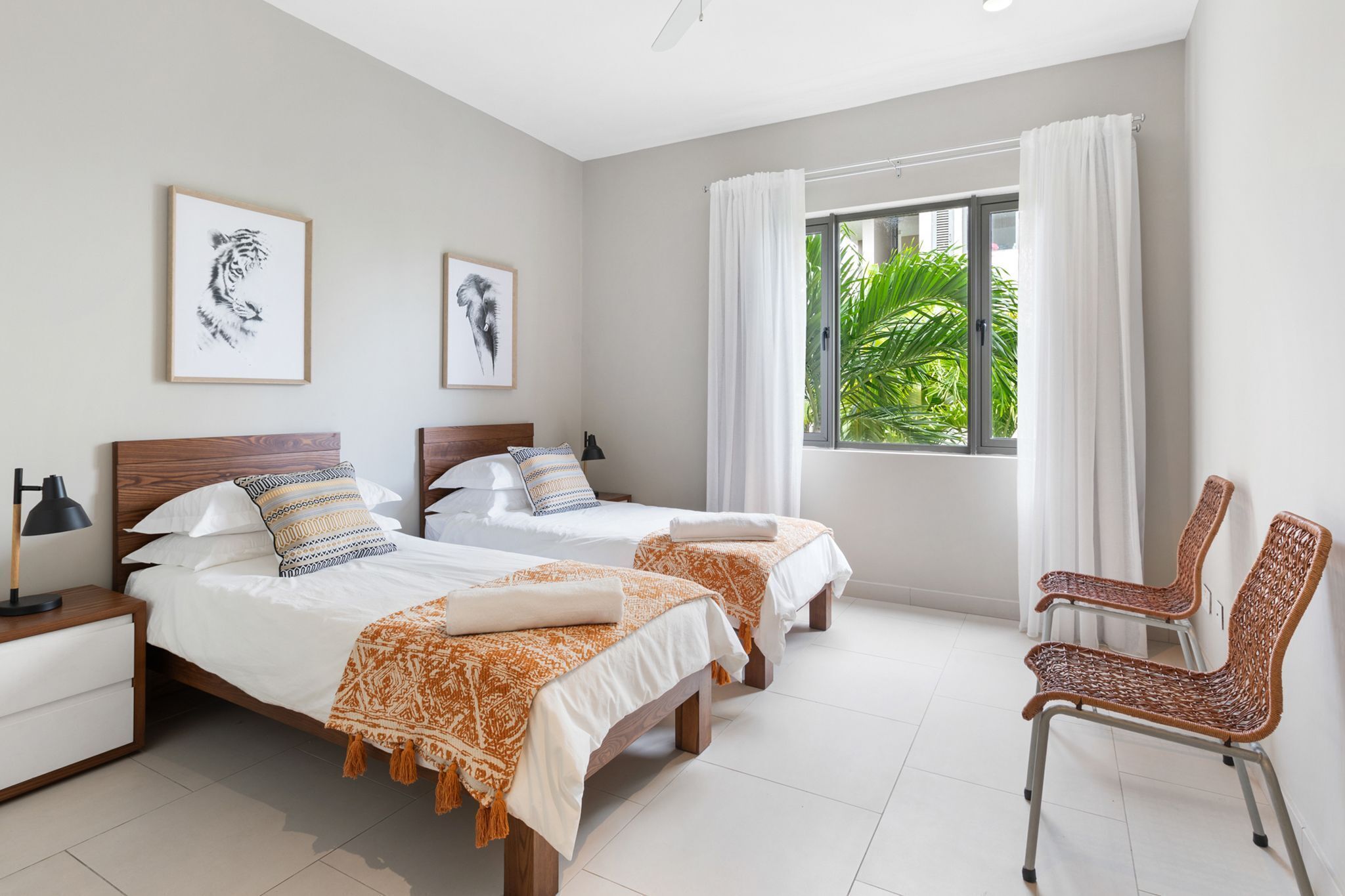 A bedroom with two beds, a chair, a nightstand, and a window with curtains.