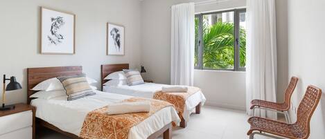 A bedroom with two beds, a chair, a nightstand, and a window with curtains.