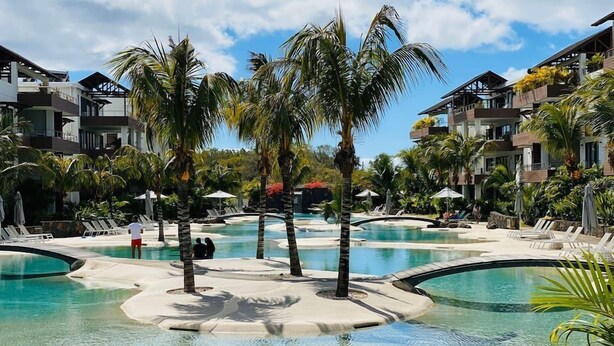 Um resort com várias piscinas, palmeiras e edifícios modernos.