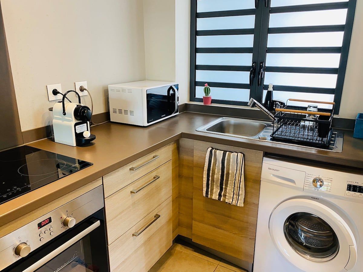 A compact kitchen with a microwave, toaster, sink, and washing machine.