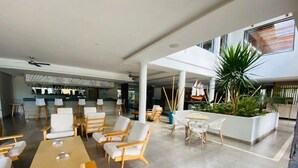 Um espaço amplo e interno com diversas opções de assento, incluindo mesas e cadeiras, e um jardim vertical central.