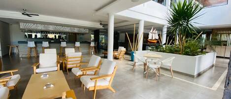 A spacious indoor area with multiple seating arrangements, including tables and chairs, and a central planter with greenery.