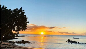 Uma praia com um pôr do sol, águas calmas e um barco ao longe.