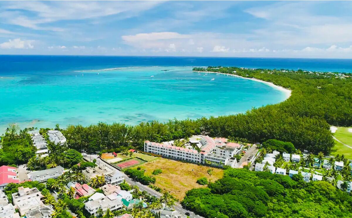 Luftaufnahme eines Küstenresorts mit einem großen Gebäude, klarem türkisblauem Wasser und üppiger Vegetation.