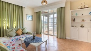 A living room with a sofa, a table with a vase, and a view to the outside. - Apartment Hibiscus (Trou aux Biches)