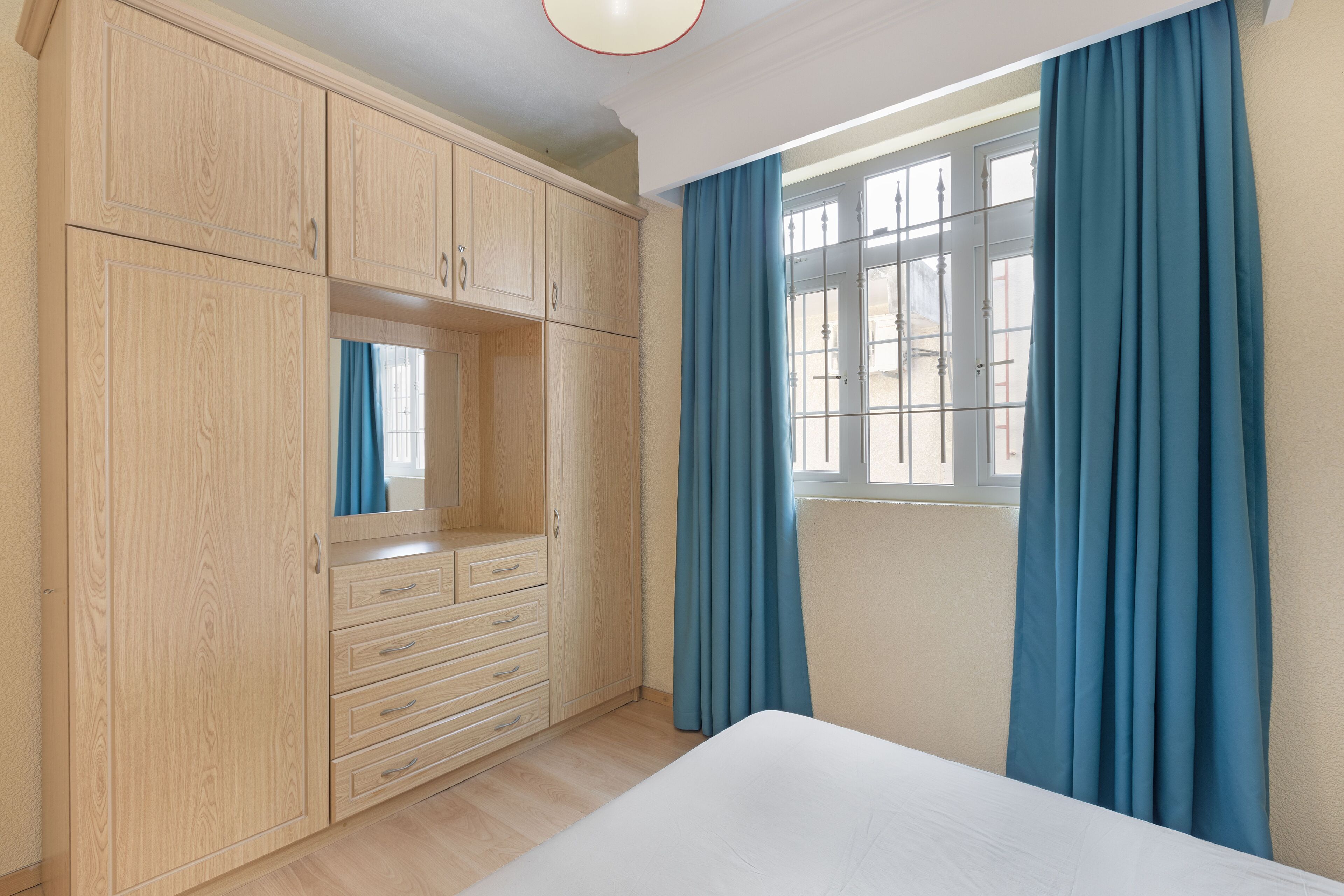 A bedroom with a large wardrobe, a bed, and a window with curtains.