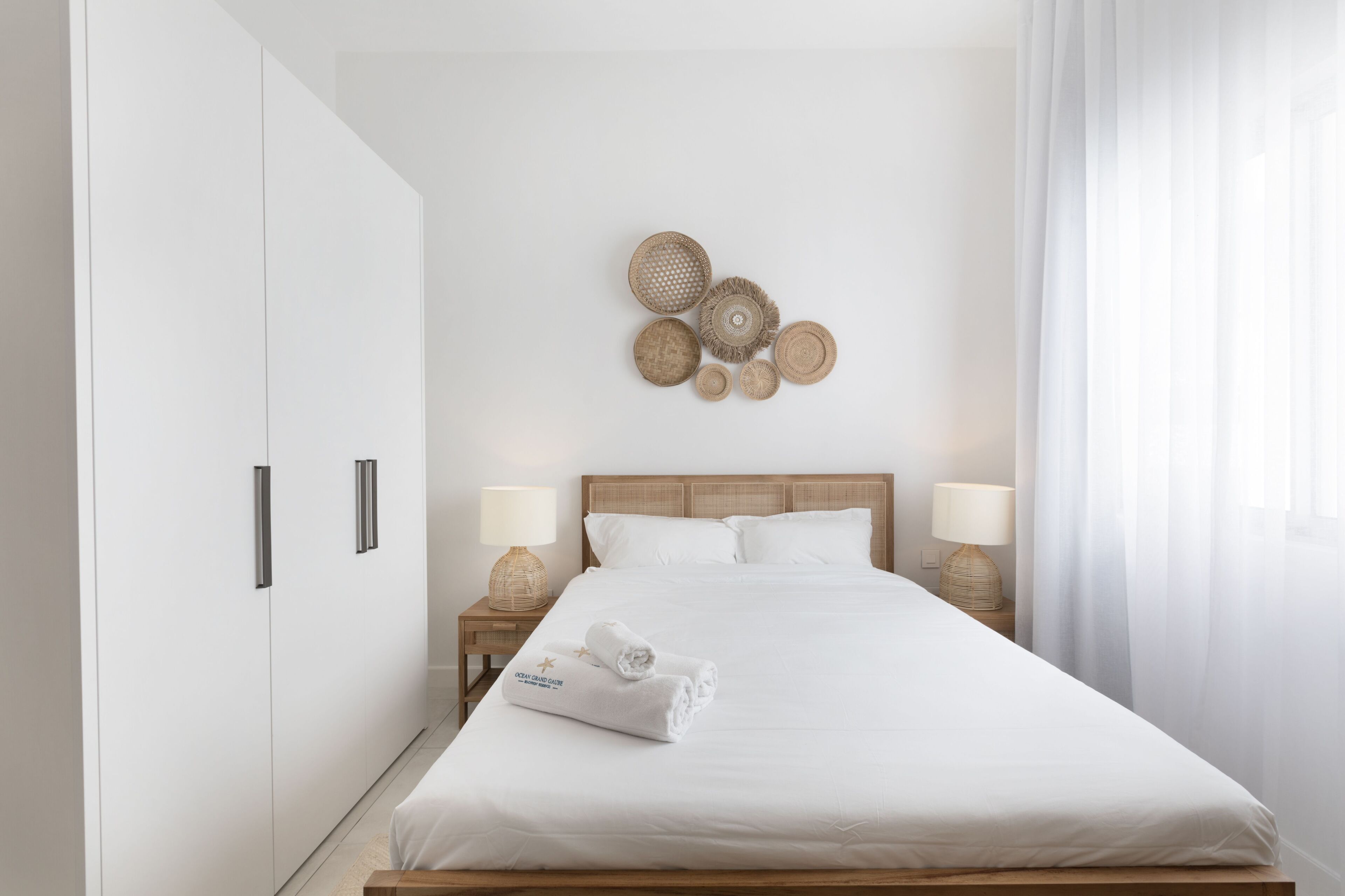 A hotel room with a large bed, two bedside tables with lamps, a wall-mounted decorative item, and a wardrobe.