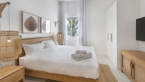 A modern bedroom with a large bed, a wooden nightstand, a TV, and a window with curtains. - Ocean Grand Gaube (Grand Gaube)