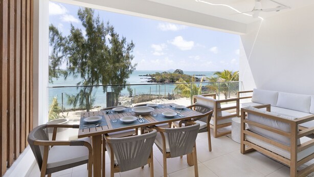A balcony with a dining table set for four, overlooking a beach and ocean. - Ocean Grand Gaube (Grand Gaube)