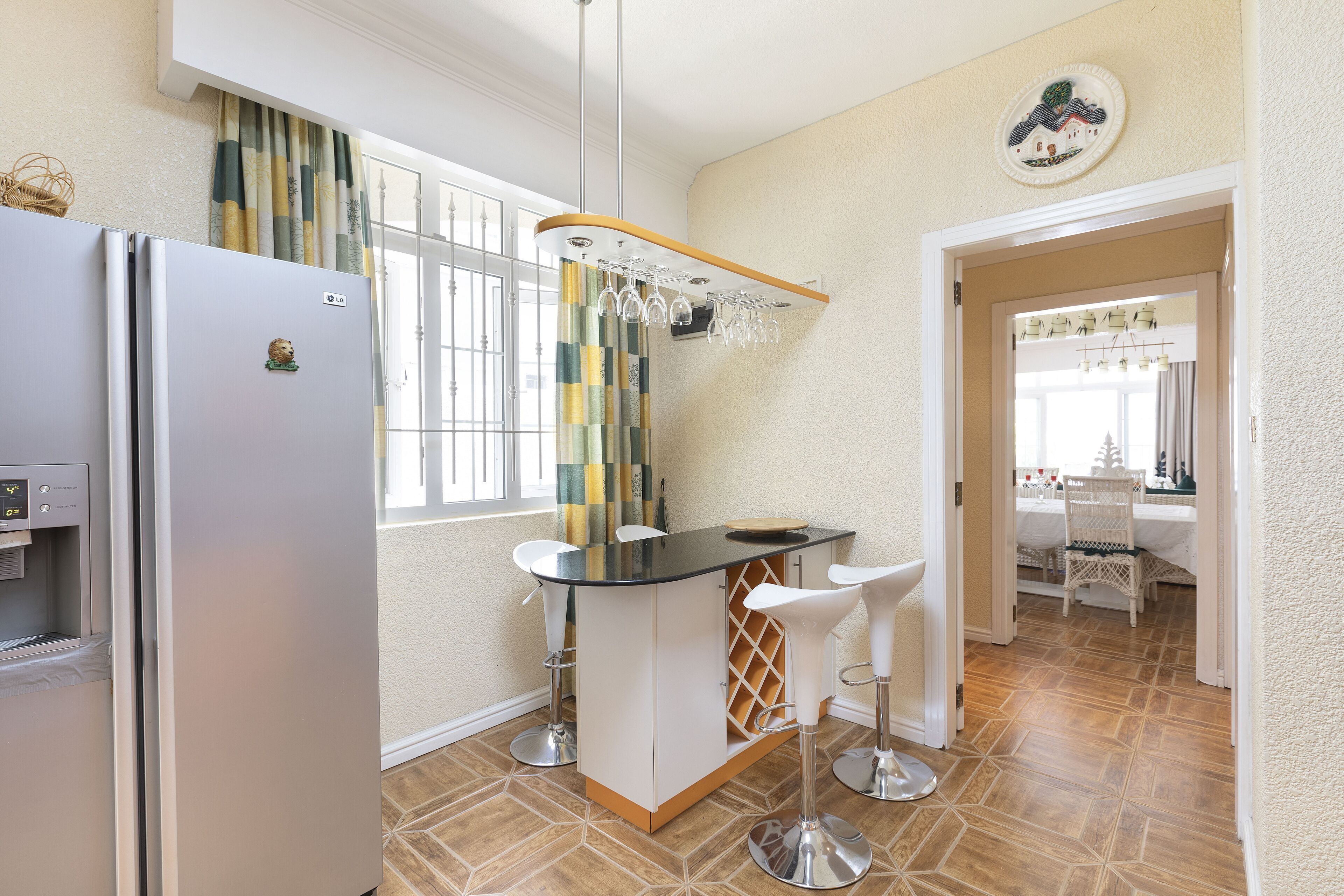 A compact kitchen with a refrigerator, a bar area with stools, and a dining area visible through an open door.