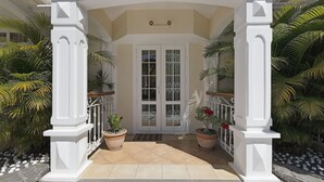 Una entrada techada con columnas blancas, puerta de vidrio y plantas en macetas.