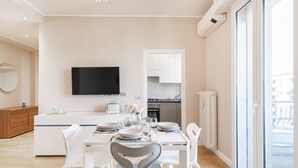 A modern kitchen with white cabinetry, a flat-screen TV mounted above the counter, and a dining area with a white table and chairs. - Easylife - View and confort in Porta Vittoria (Milano)