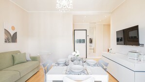 A modern dining area with a white table set for four, a green sofa, and a kitchen with a flat-screen TV. - Easylife - View and confort in Porta Vittoria (Milano)
