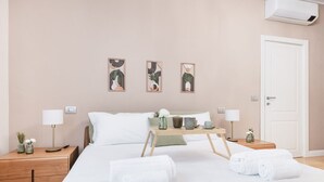 A neatly arranged hotel room with a bed, bedside tables, a bedside lamp, a tray table, and artwork on the wall. - Easylife - View and confort in Porta Vittoria (Milano)