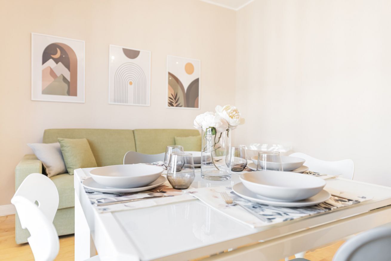 A dining area with a table set for four, a green sofa, and abstract wall art.