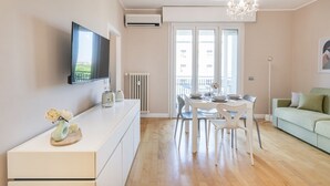 A modern living room with a dining area, a flat-screen TV mounted on the wall, a chandelier, and a green sofa. - Easylife - View and confort in Porta Vittoria (Milano)