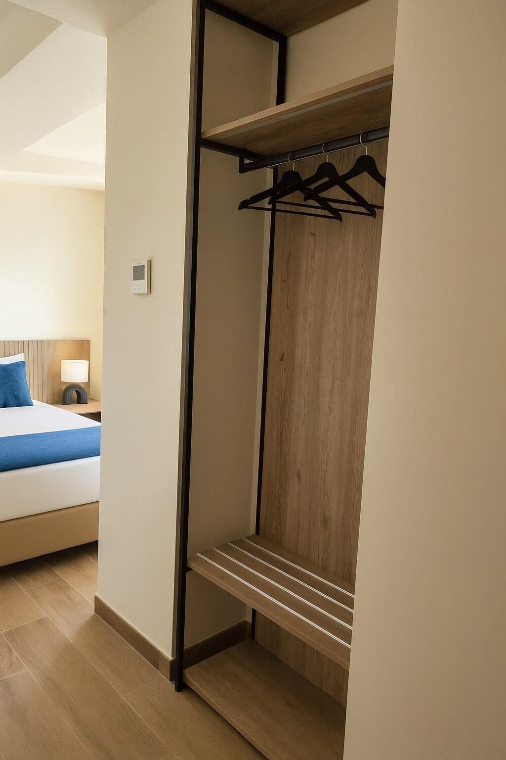 Un dormitorio con cama, mesita de noche, lámpara y un armario de madera con barra para colgar.