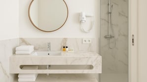 Een moderne badkamer met een marmeren wastafel, een ronde spiegel, een handdouche en een handdoekhouder.