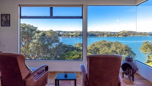 A room with large windows offering a view of a lake and surrounding trees. There are two leather chairs and a small table.