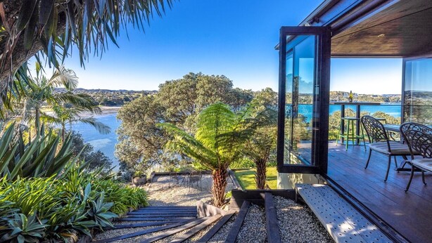A modern outdoor deck with a glass door leading to a terrace overlooking a scenic bay and hills.