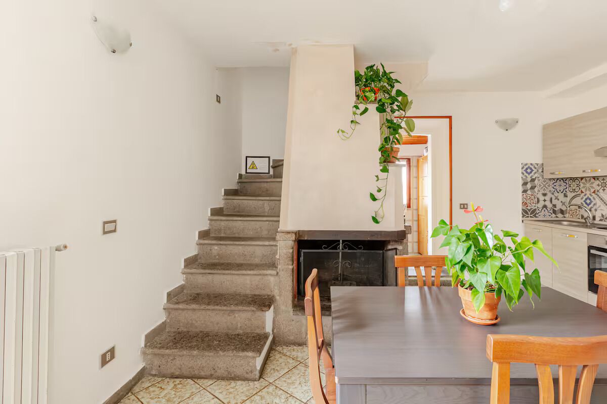 A dining area with a table and chairs, a staircase, and a kitchen in the background.