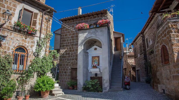 Una estrecha calle adoquinada con edificios de piedra, una pequeña escalera y plantas en macetas.