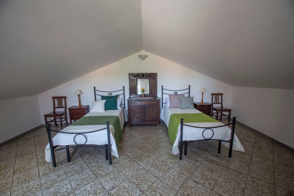 A small, triangular attic bedroom with two beds, a dresser, and a mirror.