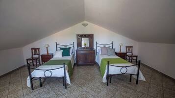 A small, triangular attic bedroom with two beds, a dresser, and a mirror.