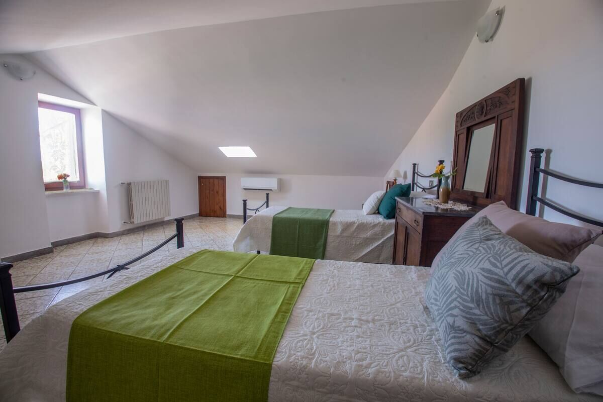 A bedroom with two beds, a window with a view, a radiator, and a mirror on the wall.