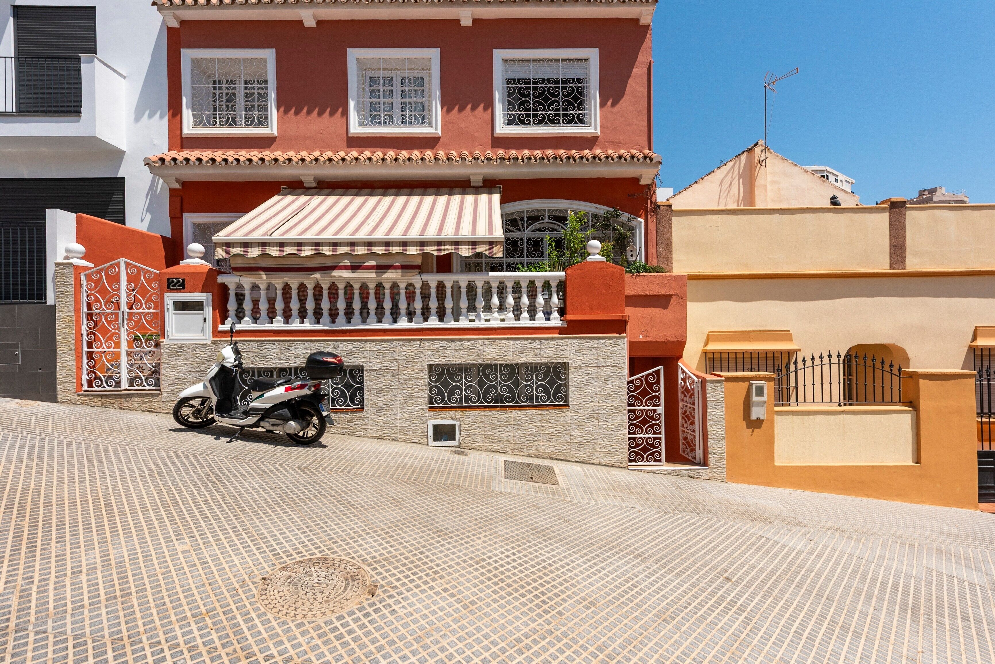 A residential building with a tiled patio, a scooter parked in front, and a gated entrance.