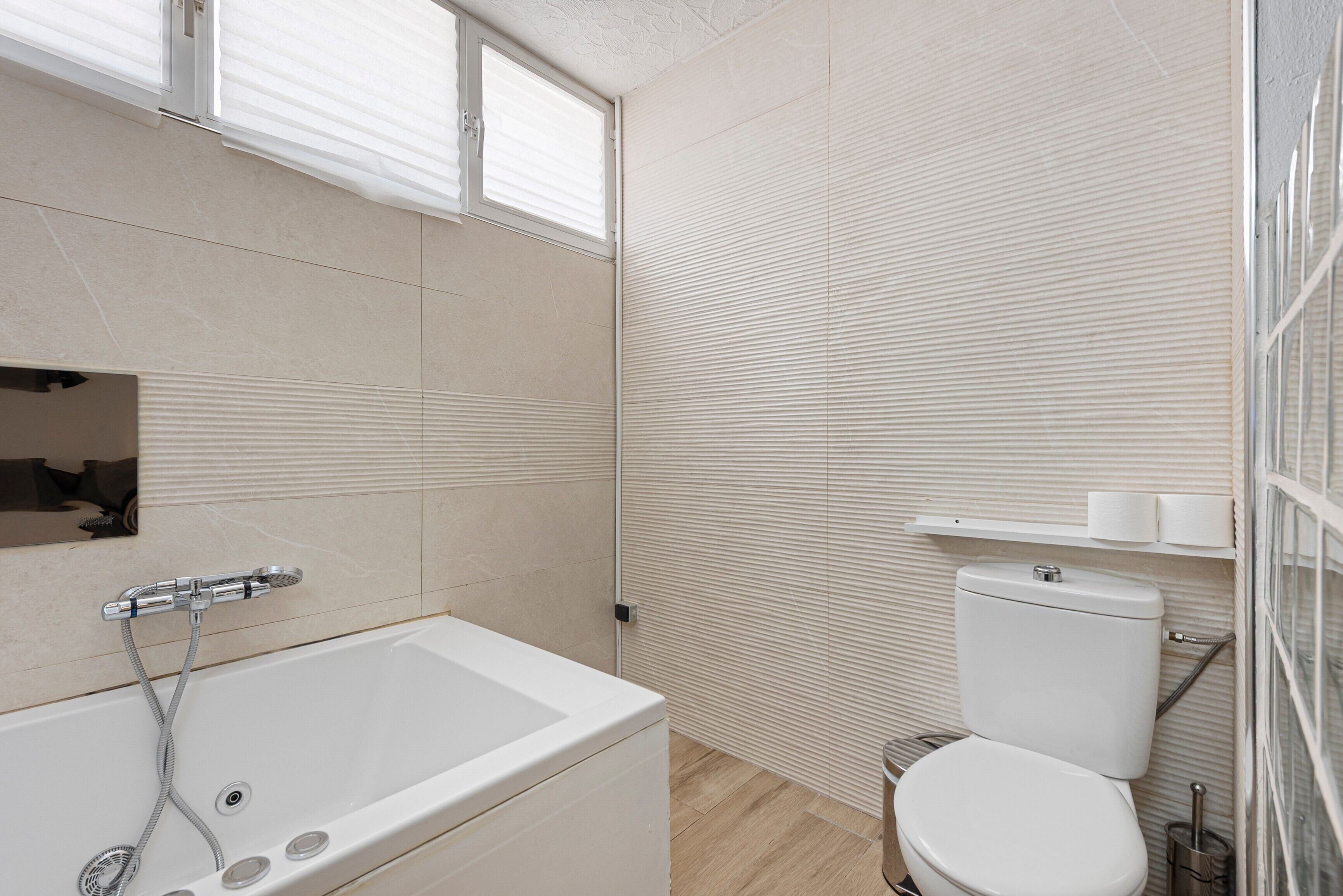 A bathroom with a bathtub, toilet, and a window.