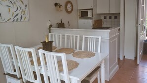 Una cocina con armarios blancos, un microondas y una estufa. Hay una mesa de comedor con sillas blancas y una botella de champán.