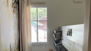 Una habitación pequeña y luminosa con una cama litera, una mesita de noche individual con lámpara, un radiador y una ventana con cortinas.