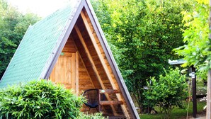Une petite structure triangulaire en bois, surmontée d’un toit vert et entourée d’une végétation luxuriante.