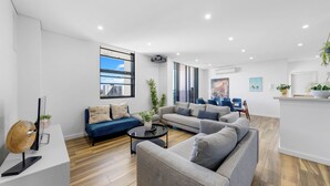A modern living room with a sofa, coffee table, and a TV on a white console. - Modern 3BR Apt w Parking near ICC & Darling Harbour (Ultimo)