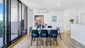 A modern dining area with a glass table, blue chairs, and a large painting of a cheetah. - Modern 3BR Apt w Parking near ICC & Darling Harbour (Ultimo)
