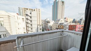 Un balcón con barandilla metálica, un pequeño armario blanco y vistas a un paisaje urbano con diversos edificios.