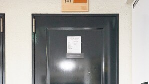 Una puerta negra con un letrero encima, un candado y una pequeña ventana rectangular.