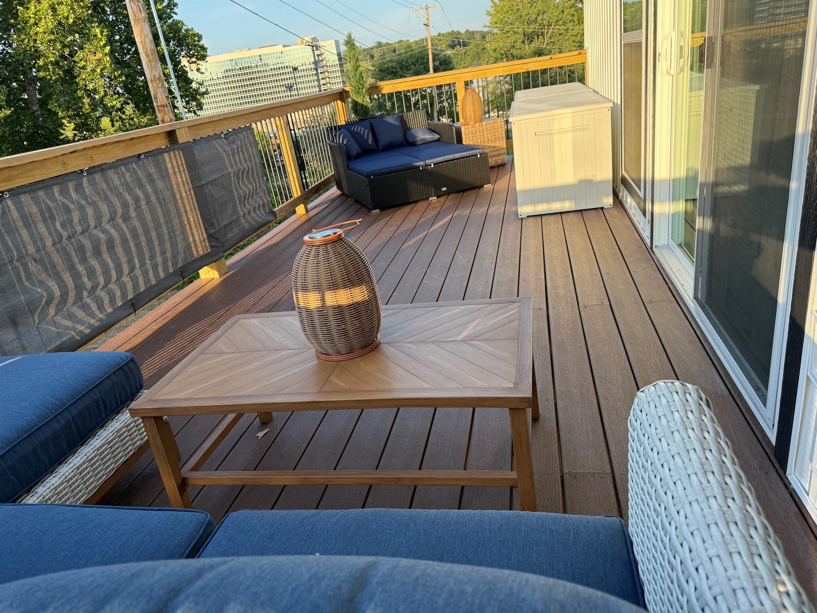 A deck with a table, a wicker chair, and a sofa with cushions.