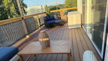 A deck with a table, a wicker chair, and a sofa with cushions.