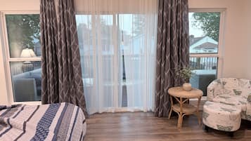 A bedroom with a bed, a chair, a small table, and a window with curtains.