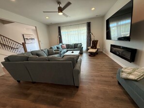 A modern living room with a sectional sofa, a recliner, a coffee table, a fireplace, and a mounted TV.