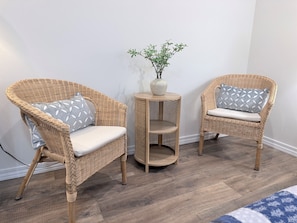 Two wicker chairs with patterned cushions, a small wooden side table with a vase, and a potted plant.