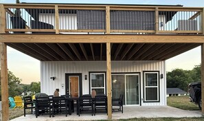 A two-story wooden deck with a covered patio area, a dining table with chairs, and a sliding glass door.