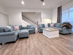 Una sala moderna con dos sofás grises, una mesa de centro de madera y una escalera al fondo.