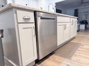 A kitchen with a stainless steel refrigerator, white cabinets, a granite countertop, and a wooden floor.