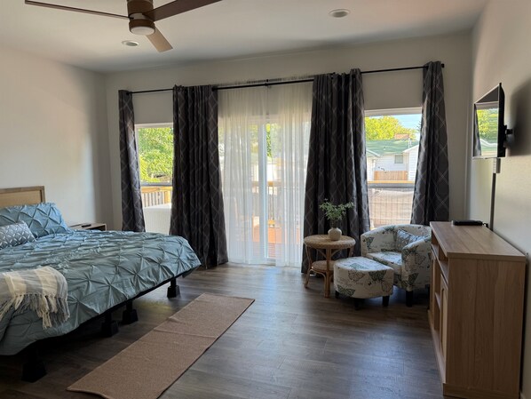 A bedroom with a bed, a small table with a plant, a sofa, and a TV on a stand.